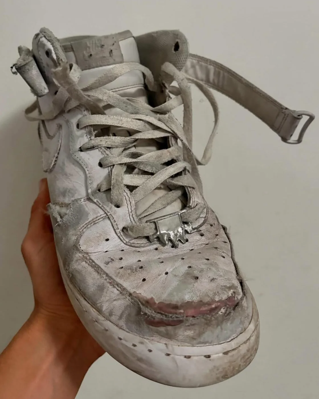 A white high top held in one hand, with a cast silver plate fitted over the lacing