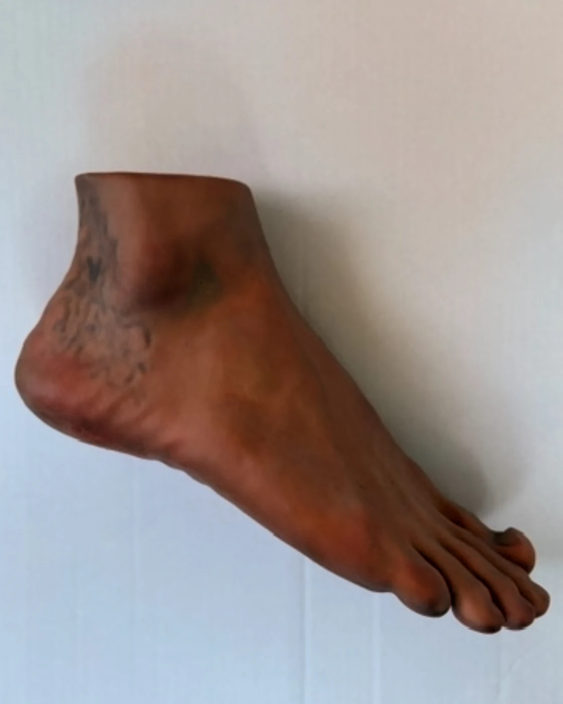 A cast foot lying on its side against a pale board, tattooed across the ankle