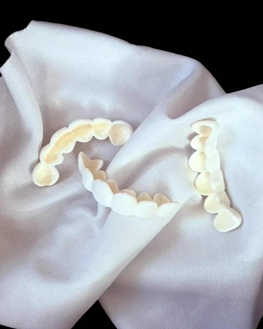 Two sets of grillz cast in porcelain, upper and lower, close in the folds of a white cloth