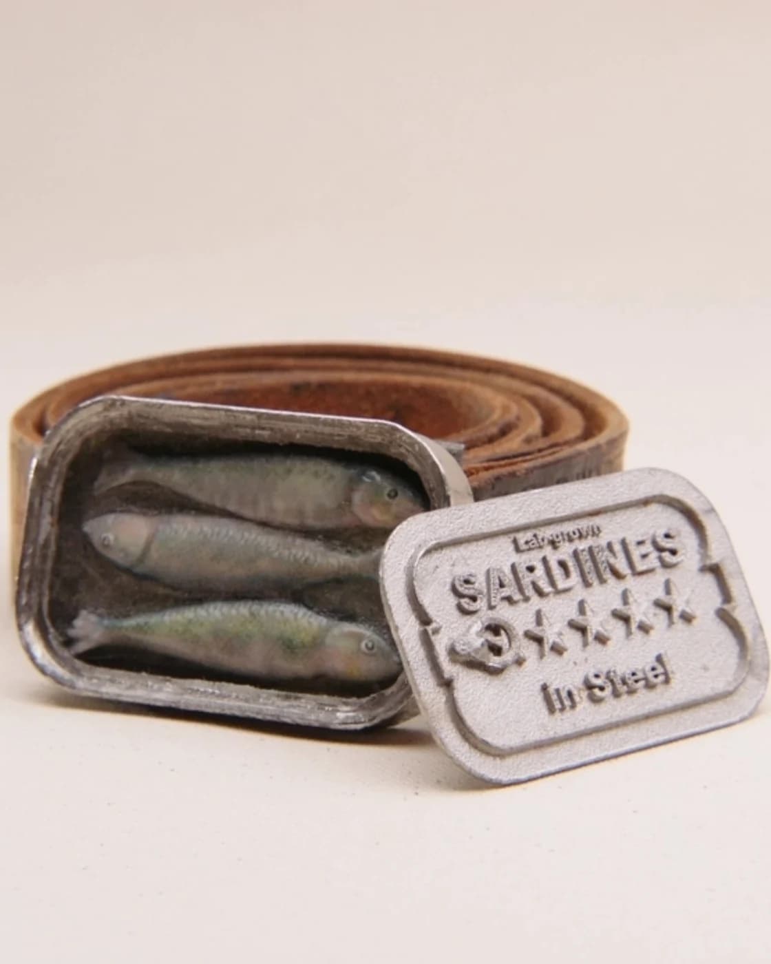 The sardine buckle open, three cast fish lying in the tin and the stamped lid standing beside it