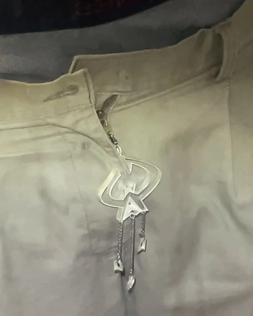 The zipper piece worn, hanging from the fly of a pair of trousers